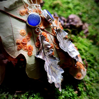 Earrings with blue sea glass and leaf-like elements on a mossy background
