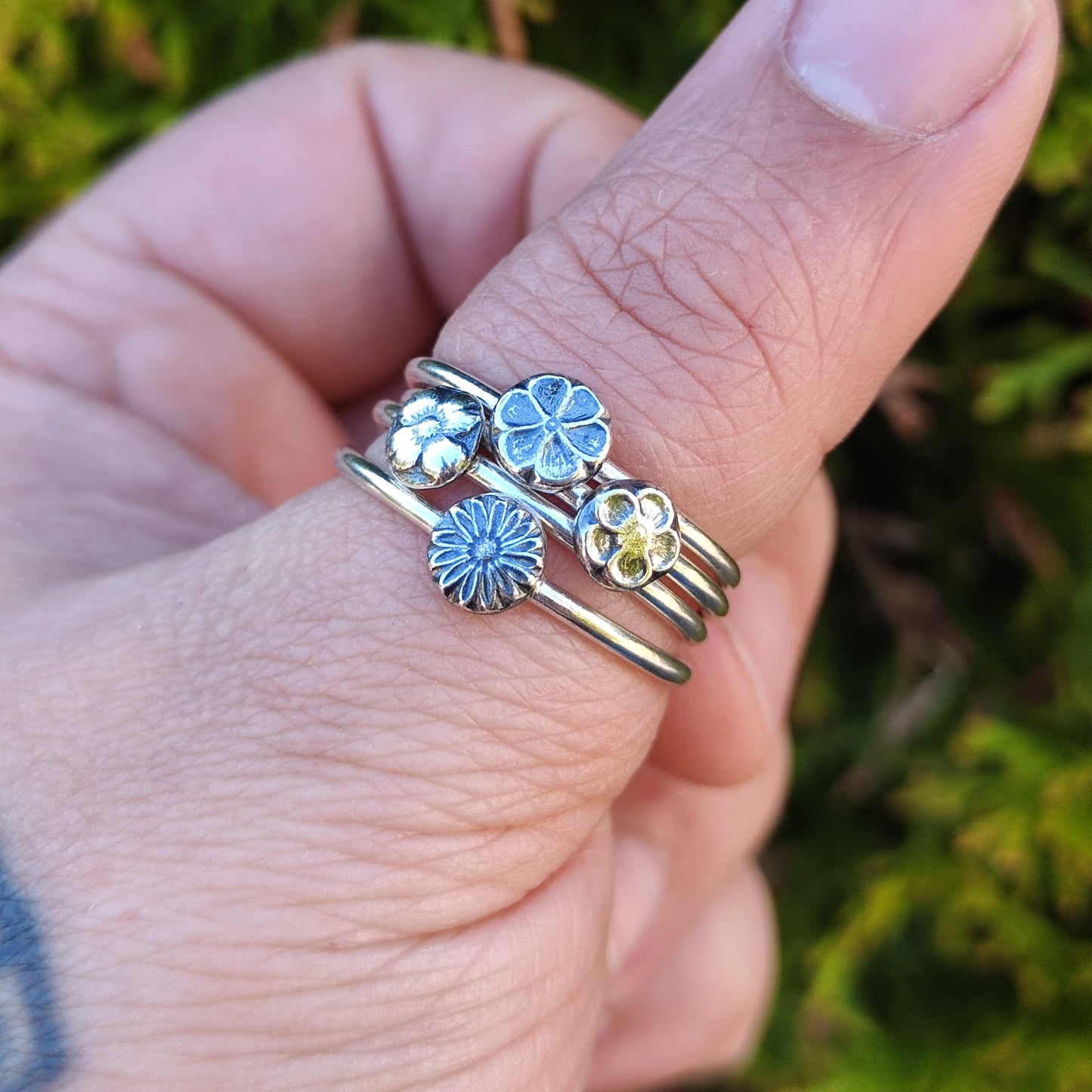 Set of Stacker Rings with flower motifs made from 100% recycled silver being worn on the thumb.