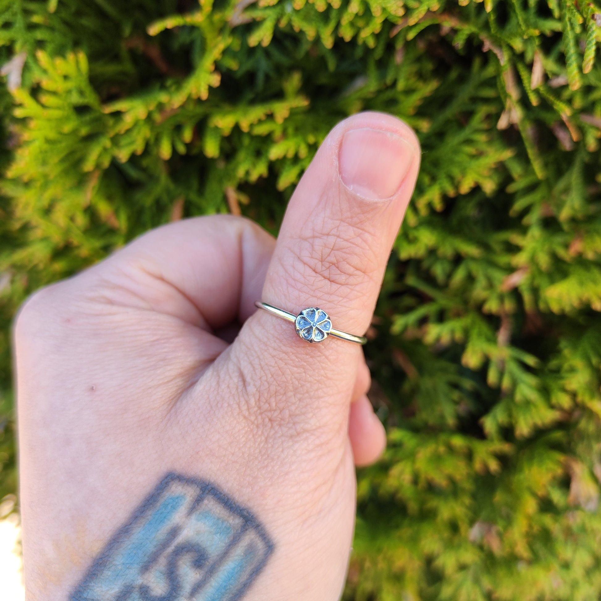 100% recycled silver stacker ring with a 6-petal flower design being worn on the thumb. 
