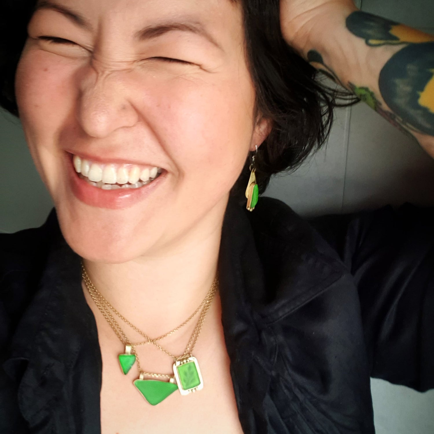 Person wearing green jewelry with a tattooed arm in the background